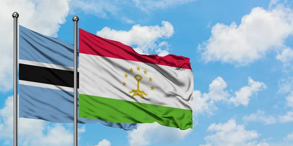 Bandera de Botswana y Tayikistán ondeando en el viento contra el cielo azul nublado blanco juntos. Concepto diplomático, relaciones internacionales . — Foto de Stock