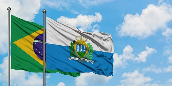 O Brasil e a bandeira de San Marino agitando no vento contra o céu azul nublado branco juntos. Conceito de diplomacia, relações internacionais . — Fotografia de Stock