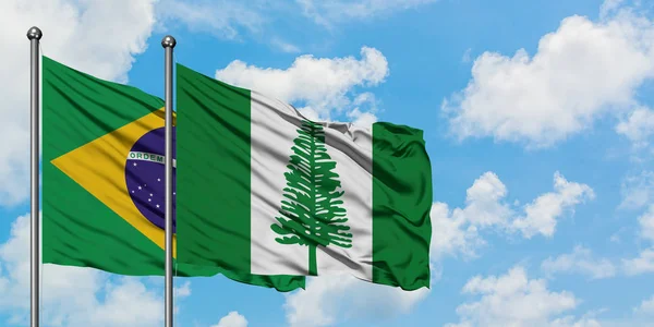 Bandera de Brasil y Norfolk Island ondeando en el viento contra el cielo azul nublado blanco juntos. Concepto diplomático, relaciones internacionales . — Foto de Stock