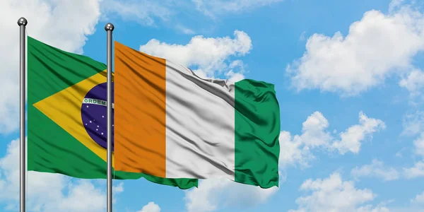 Drapeau du Brésil et de la Côte d'Ivoire agitant dans le vent contre ciel bleu nuageux blanc ensemble. Concept de diplomatie, relations internationales . — Photo