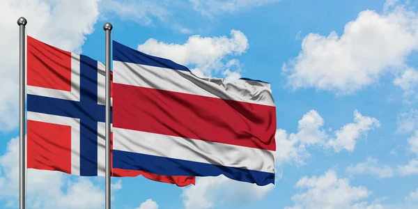 Bandera de las Islas Bouvet y Costa Rica ondeando en el viento contra el cielo azul nublado blanco juntos. Concepto diplomático, relaciones internacionales . — Foto de Stock