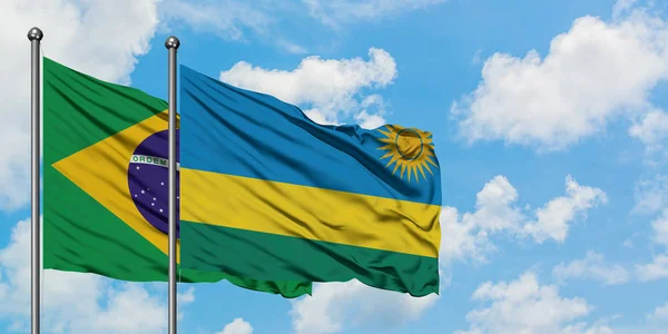 Bandera de Brasil y Ruanda ondeando en el viento contra el cielo azul nublado blanco juntos. Concepto diplomático, relaciones internacionales . — Foto de Stock