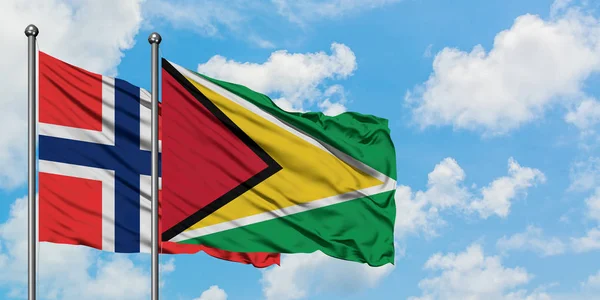 Bandera de las islas Bouvet y Guyana ondeando en el viento contra el cielo azul nublado blanco juntos. Concepto diplomático, relaciones internacionales . — Foto de Stock