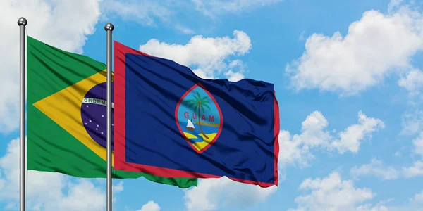 Bandera de Brasil y Guam ondeando en el viento contra el cielo azul nublado blanco juntos. Concepto diplomático, relaciones internacionales . — Foto de Stock