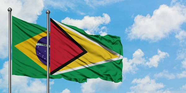 Bandera de Brasil y Guyana ondeando en el viento contra el cielo azul nublado blanco juntos. Concepto diplomático, relaciones internacionales . — Foto de Stock