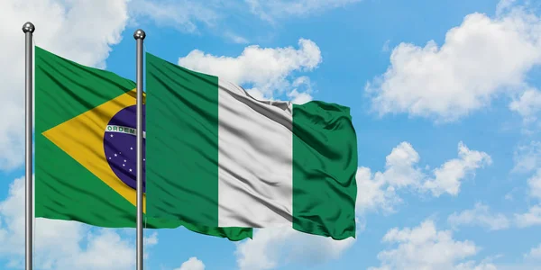 Bandeira do Brasil e Nigéria agitando no vento contra o céu azul nublado branco juntos. Conceito de diplomacia, relações internacionais . — Fotografia de Stock