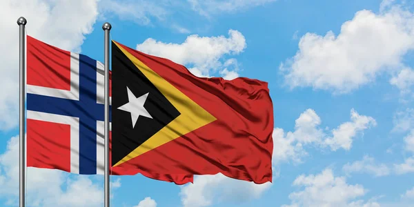 Islas Bouvet y la bandera de Timor Oriental ondeando en el viento contra el cielo azul nublado blanco juntos. Concepto diplomático, relaciones internacionales . — Foto de Stock