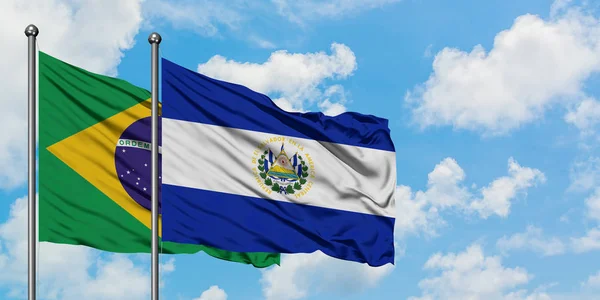 O Brasil e a bandeira de El Salvador agitando no vento contra o céu azul nublado branco juntos. Conceito de diplomacia, relações internacionais . — Fotografia de Stock