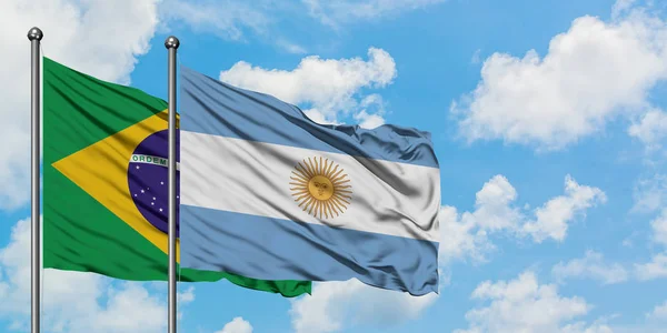 Bandeira do Brasil e da Argentina agitando no vento contra o céu azul nublado branco juntos. Conceito de diplomacia, relações internacionais . — Fotografia de Stock