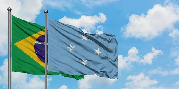 Bandera de Brasil y Micronesia ondeando en el viento contra el cielo azul nublado blanco juntos. Concepto diplomático, relaciones internacionales . — Foto de Stock