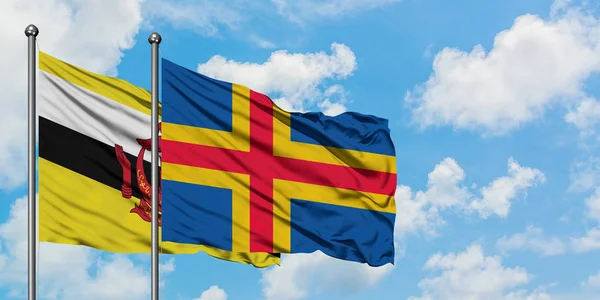 Bandera de Brunéi y las Islas Aland ondeando en el viento contra el cielo azul nublado blanco juntos. Concepto diplomático, relaciones internacionales . — Foto de Stock