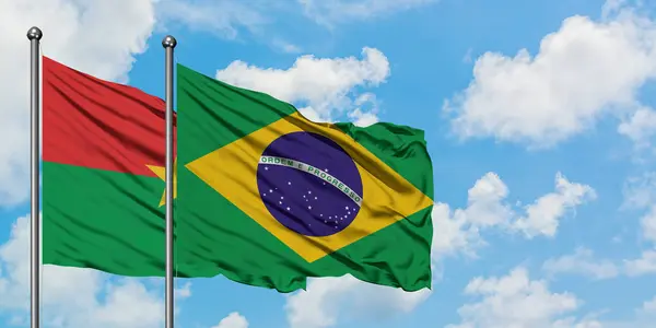 Burkina Faso y la bandera de Brasil ondeando en el viento contra el cielo azul nublado blanco juntos. Concepto diplomático, relaciones internacionales . — Foto de Stock