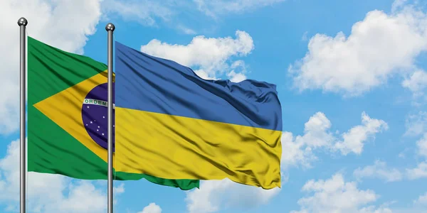 Bandera de Brasil y Ucrania ondeando en el viento contra el cielo azul nublado blanco juntos. Concepto diplomático, relaciones internacionales . — Foto de Stock