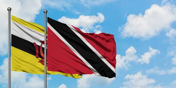 Brunei e a bandeira de Trinidad e Tobago agitando no vento contra o céu azul nublado branco juntos. Conceito de diplomacia, relações internacionais . — Fotografia de Stock