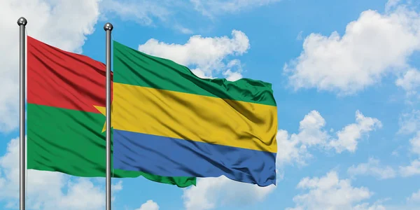 Burkina Faso e Gabon sventolano nel vento contro il bianco cielo blu nuvoloso insieme. Concetto di diplomazia, relazioni internazionali . — Foto Stock