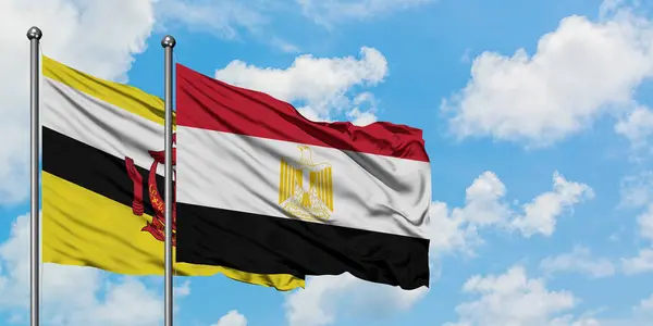 Brunei y la bandera de Egipto ondeando en el viento contra el cielo azul nublado blanco juntos. Concepto diplomático, relaciones internacionales . — Foto de Stock