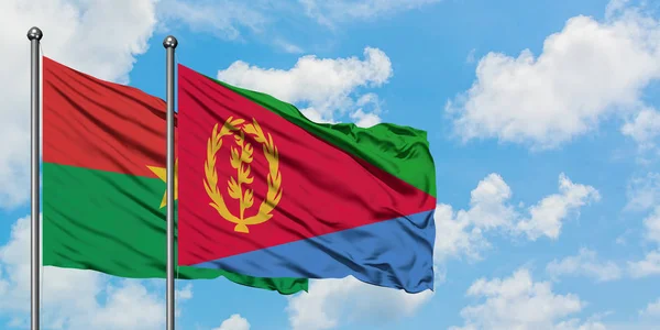 Burkina Faso y la bandera de Eritrea ondeando en el viento contra el cielo azul nublado blanco juntos. Concepto diplomático, relaciones internacionales . — Foto de Stock