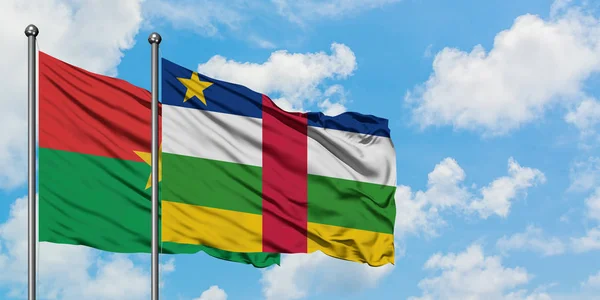 Burkina Faso y la bandera de la República Centroafricana ondeando en el viento contra el cielo azul nublado blanco juntos. Concepto diplomático, relaciones internacionales . — Foto de Stock