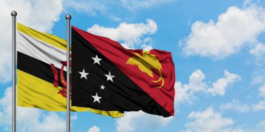 Brunei ve Papua Yeni Gine bayrağı birlikte beyaz bulutlu mavi gökyüzüne karşı rüzgarda sallayarak. Diplomasi kavramı, uluslararası ilişkiler.