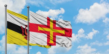 Brunei ve Guernsey bayrağı birlikte beyaz bulutlu mavi gökyüzüne karşı rüzgarda sallayarak. Diplomasi kavramı, uluslararası ilişkiler.