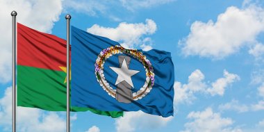 Burkina Faso ve Kuzey Mariana Adaları bayrağı birlikte beyaz bulutlu mavi gökyüzüne karşı rüzgarda sallayarak. Diplomasi kavramı, uluslararası ilişkiler.