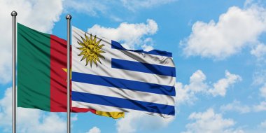 Kamerun ve Uruguay bayrağı birlikte beyaz bulutlu mavi gökyüzüne karşı rüzgarsal sallayarak. Diplomasi kavramı, uluslararası ilişkiler.