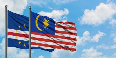 Cape Verde ve Malezya bayrağı birlikte beyaz bulutlu mavi gökyüzüne karşı rüzgarda sallayarak. Diplomasi kavramı, uluslararası ilişkiler.