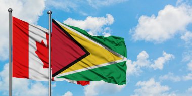 Kanada ve Guyana bayrağı birlikte beyaz bulutlu mavi gökyüzüne karşı rüzgarda sallayarak. Diplomasi kavramı, uluslararası ilişkiler.