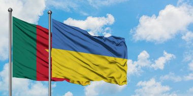 Kamerun ve Ukrayna bayrağı birlikte beyaz bulutlu mavi gökyüzüne karşı rüzgarda sallayarak. Diplomasi kavramı, uluslararası ilişkiler.