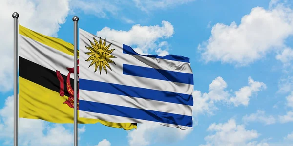 Bandera de Brunei y Uruguay ondeando en el viento contra el cielo azul nublado blanco juntos. Concepto diplomático, relaciones internacionales . —  Fotos de Stock