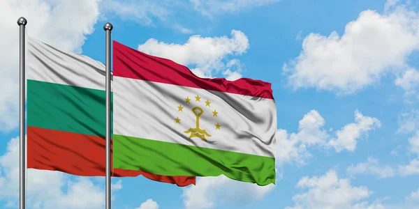 Bandera de Bulgaria y Tayikistán ondeando en el viento contra el cielo azul nublado blanco juntos. Concepto diplomático, relaciones internacionales . — Foto de Stock