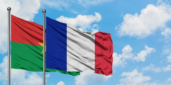 Burkina Faso y la bandera de Francia ondeando en el viento contra el cielo azul nublado blanco juntos. Concepto diplomático, relaciones internacionales . — Foto de Stock