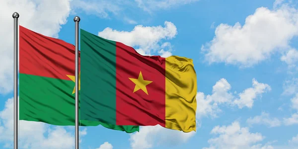 Burkina Faso y la bandera de Camerún ondeando en el viento contra el cielo azul nublado blanco juntos. Concepto diplomático, relaciones internacionales . — Foto de Stock