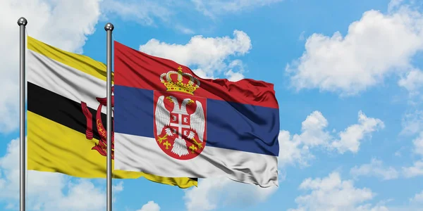Bandera de Brunéi y Serbia ondeando en el viento contra el cielo azul nublado blanco juntos. Concepto diplomático, relaciones internacionales . — Foto de Stock