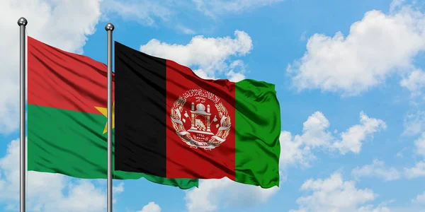 Burkina Faso y la bandera de Afganistán ondeando en el viento contra el cielo azul nublado blanco juntos. Concepto diplomático, relaciones internacionales . — Foto de Stock