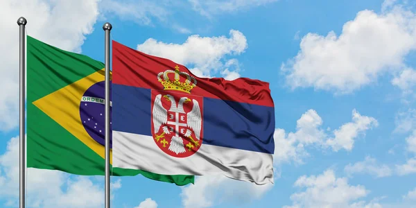 Bandera de Brasil y Serbia ondeando en el viento contra el cielo azul nublado blanco juntos. Concepto diplomático, relaciones internacionales . — Foto de Stock