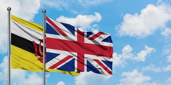 Brunej a Velká Británie vlajkami mávali ve větru proti bíle zatažené modré obloze. Diplomacie, mezinárodní vztahy. — Stock fotografie