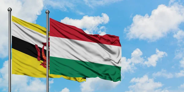 Bandera de Brunéi y Hungría ondeando en el viento contra el cielo azul nublado blanco juntos. Concepto diplomático, relaciones internacionales . — Foto de Stock