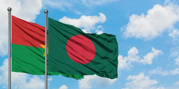 Burkina Faso y la bandera de Bangladesh ondeando en el viento contra el cielo azul nublado blanco juntos. Concepto diplomático, relaciones internacionales . — Foto de Stock