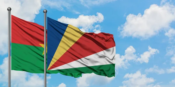 Le Burkina Faso et les Seychelles battent ensemble dans le vent contre un ciel bleu nuageux blanc. Concept de diplomatie, relations internationales . — Photo