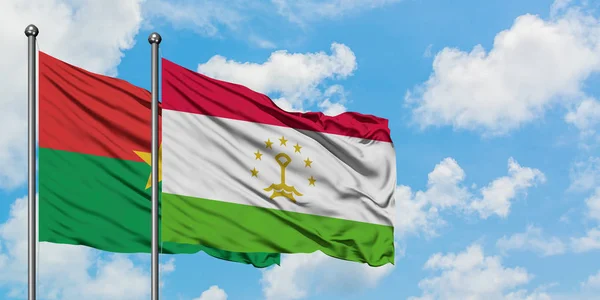Bandera de Burkina Faso y Tayikistán ondeando en el viento contra el cielo azul nublado blanco juntos. Concepto diplomático, relaciones internacionales . — Foto de Stock