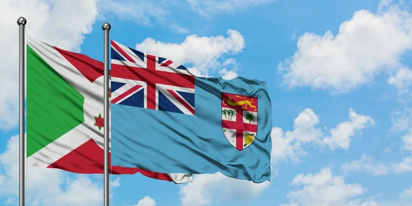 Bandera de Burundi y Fiyi ondeando en el viento contra el cielo azul nublado blanco juntos. Concepto diplomático, relaciones internacionales . — Foto de Stock