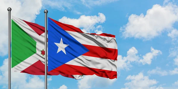 Bandera de Burundi y Puerto Rico ondeando en el viento contra el cielo azul nublado blanco juntos. Concepto diplomático, relaciones internacionales . — Foto de Stock