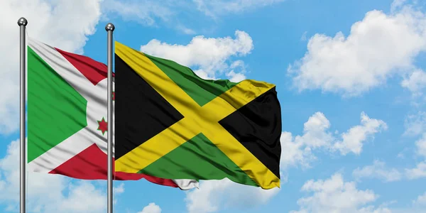 Bandera de Burundi y Jamaica ondeando en el viento contra el cielo azul nublado blanco juntos. Concepto diplomático, relaciones internacionales . — Foto de Stock