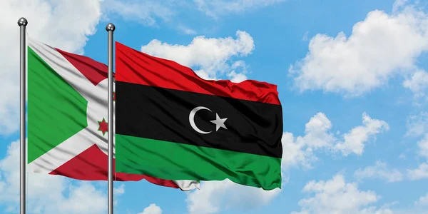 Bandera de Burundi y Libia ondeando en el viento contra el cielo azul nublado blanco juntos. Concepto diplomático, relaciones internacionales . — Foto de Stock