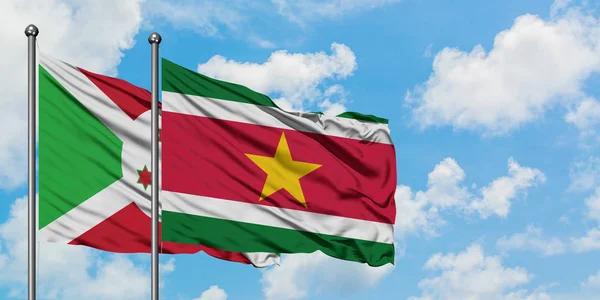 Bandera de Burundi y Surinam ondeando en el viento contra el cielo azul nublado blanco juntos. Concepto diplomático, relaciones internacionales . — Foto de Stock