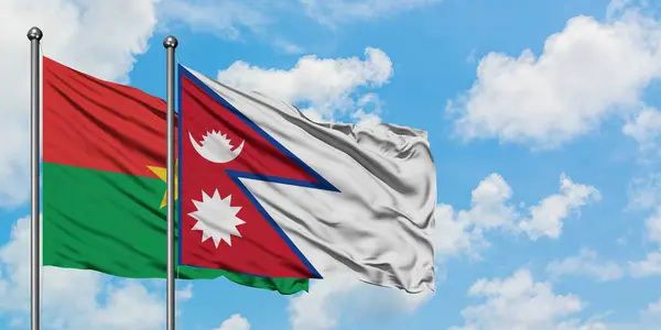 Burkina Faso y la bandera de Nepal ondeando en el viento contra el cielo azul nublado blanco juntos. Concepto diplomático, relaciones internacionales . — Foto de Stock