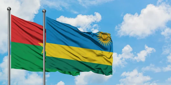 Burkina Faso y la bandera de Ruanda ondeando en el viento contra el cielo azul nublado blanco juntos. Concepto diplomático, relaciones internacionales . — Foto de Stock