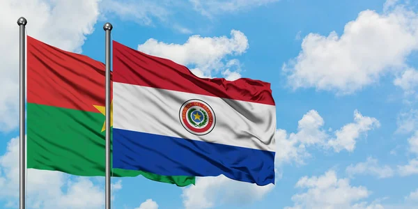 Burkina Faso y la bandera de Paraguay ondeando en el viento contra el cielo azul nublado blanco juntos. Concepto diplomático, relaciones internacionales . — Foto de Stock