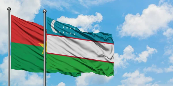 Bandera de Burkina Faso y Uzbekistán ondeando en el viento contra el cielo azul nublado blanco juntos. Concepto diplomático, relaciones internacionales . — Foto de Stock